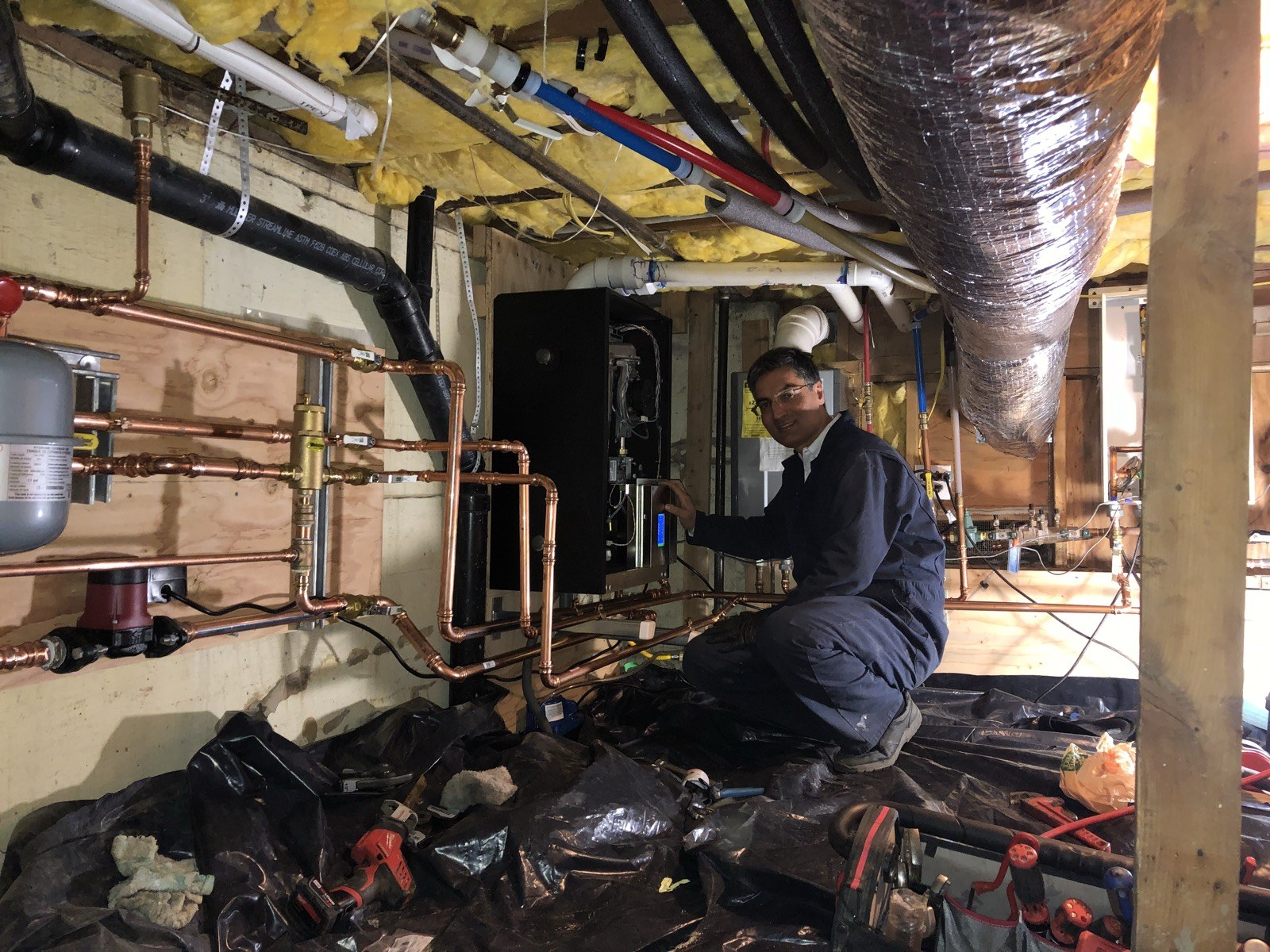 Mehran kneeling beside an open heating appliance and copper pipework on site