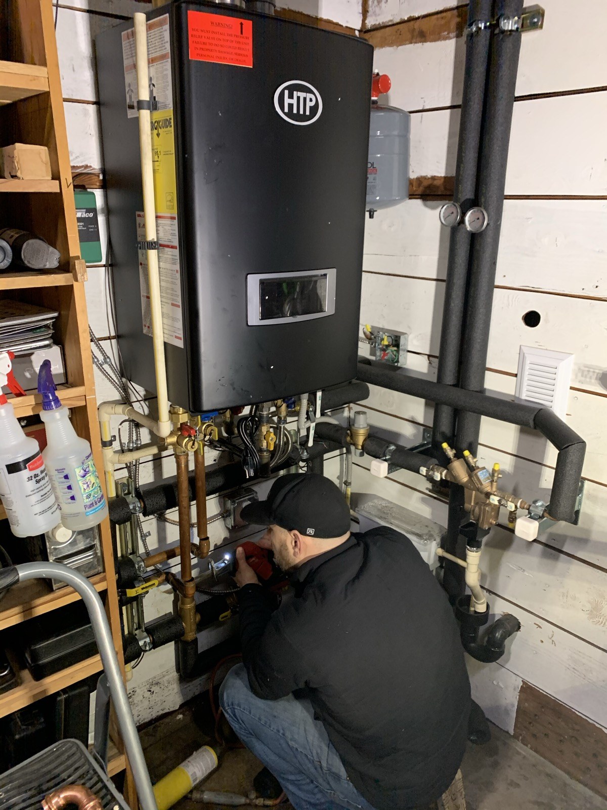 Technician working on pipework beneath a wall-mounted HTP heating appliance