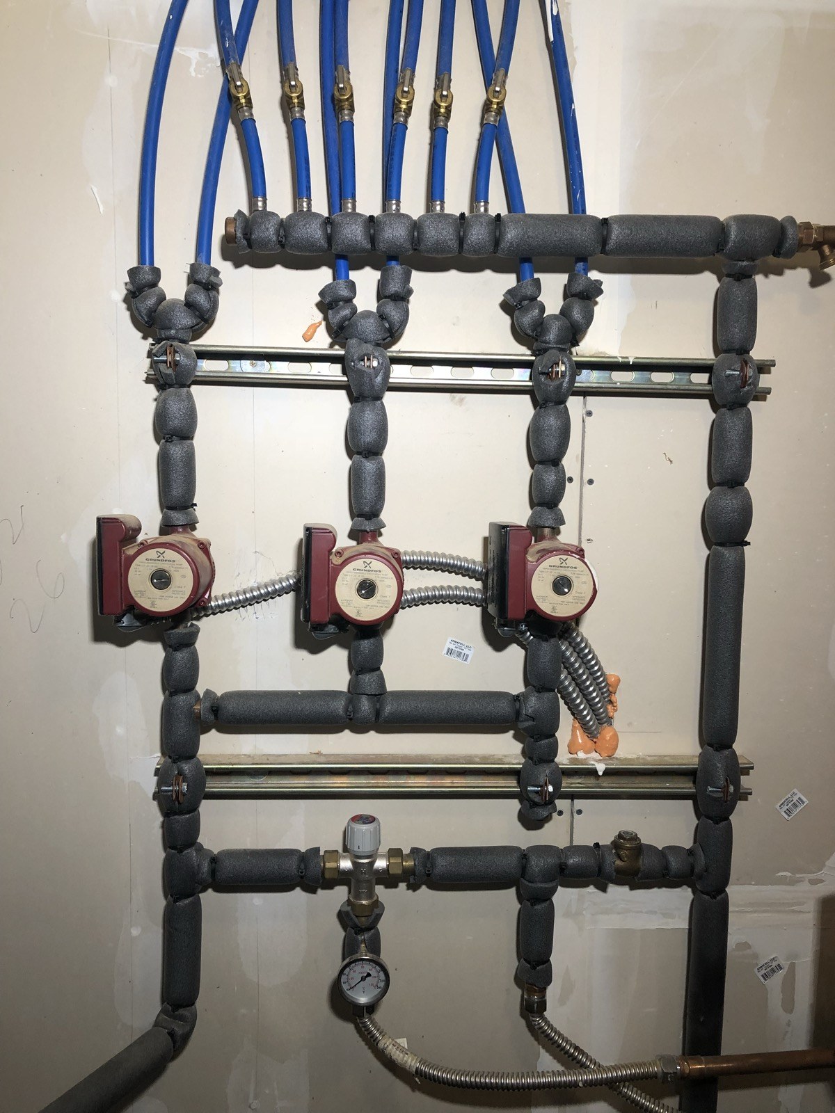 Three hydronic circulation pumps with insulated headers and blue pipe branches