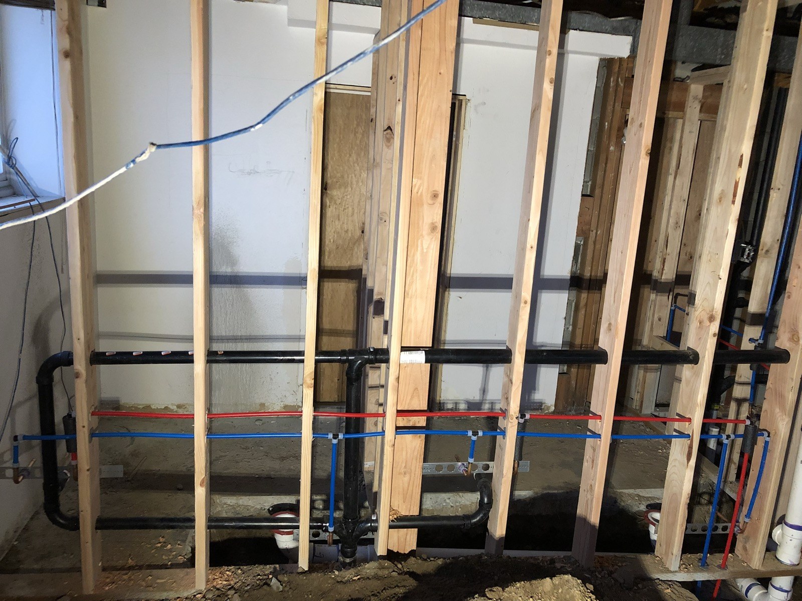 Red and blue supply pipes with black drain pipes in wall framing