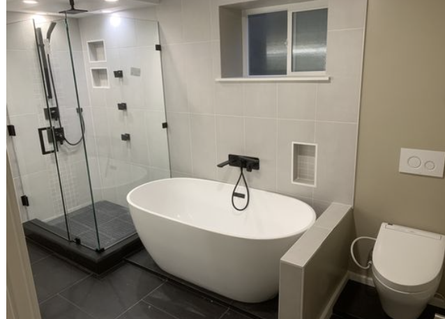 Freestanding white bathtub, glass shower enclosure and wall-hung toilet in a tiled bathroom